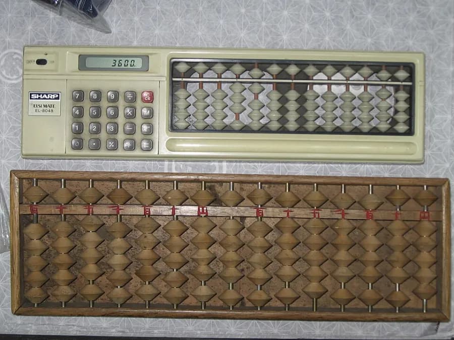 A wooden Japanese abacus with rows of beads, next to an electronic calculator, on a shop counter.