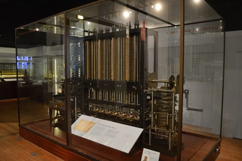A large mechanical calculating machine made of brass gears and columns, displayed in a glass case in a museum.